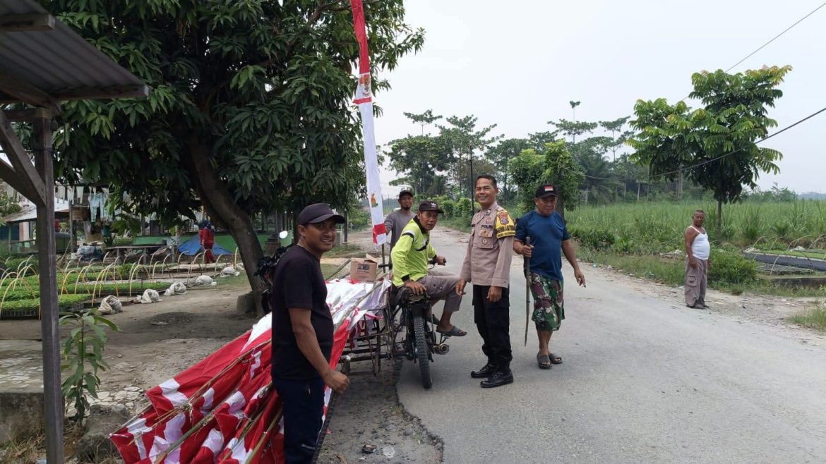 Bhabinkamtibmas Polsek Secanggang Bersama Aparatur Desa Pasang Umbul-Umbul dan Imbau Warga Kibarkan Bendera Merah Putih.